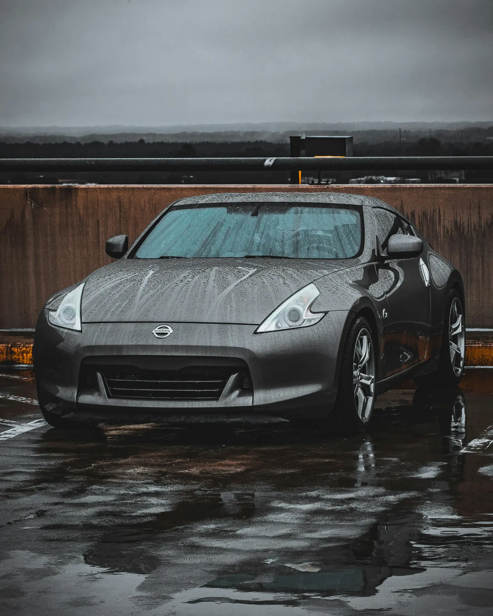 Nissan 370Z beaded with rain in front of a weathered timber wall